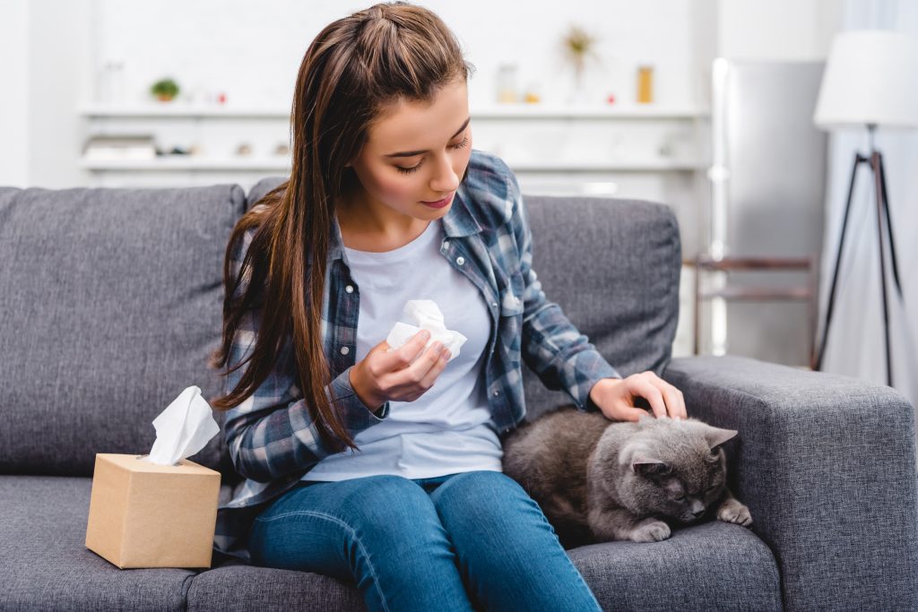 Mujer con síntomas de alergia acariciando a un gato mientras sostiene un pañuelo.